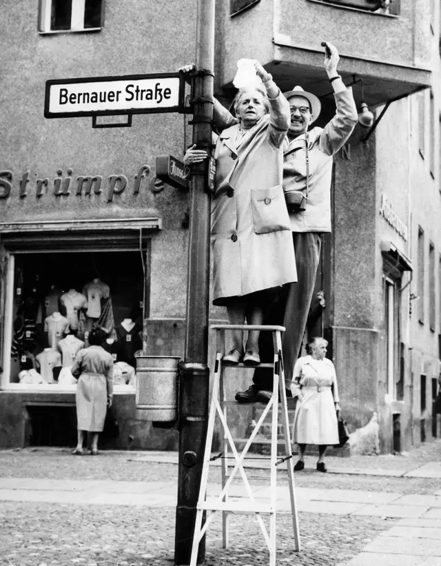 pessoas penduradas numa placa da Bernauer Strasse