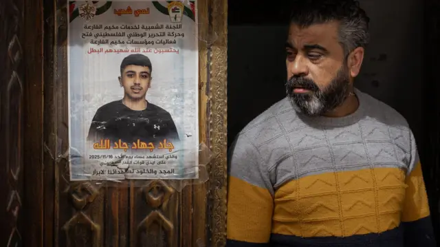 Ojciec Jada stoi obok plakatu upamiętniającego jego syna, przyklejonego do rzeźbionych drewnianych drzwi wejściowych domu w obozie dla uchodźców Al-Far'a na okupowanym Zachodnim Brzegu