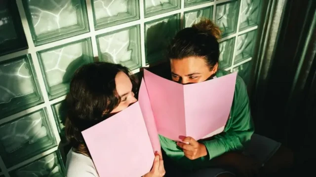 Две девојке се смеју и прекривају лице розе листовима