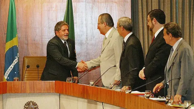 Lula e José Dirceu apertam as mãos, de pé, em um gabinete.