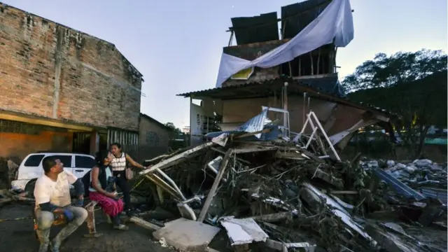 நிலச்சரிவால் இடிந்துபோன வீட்டிற்கு முன்னால் குடும்பத்தினர்