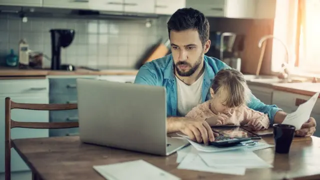 Pai trabalha no computador com a filha no colo