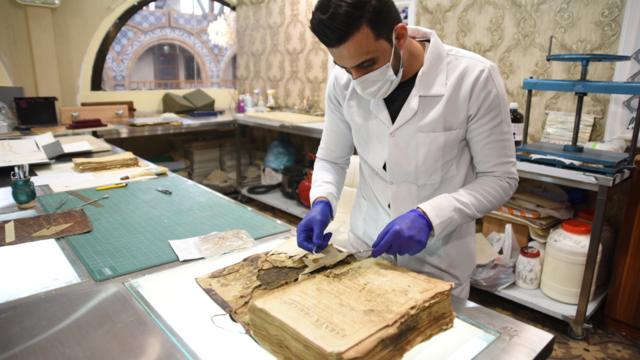 النجف - فني يقوم بترميم مخطوطة مسيحية قديمة في منشأة متخصصة بترميم المخطوطات في النجف استعدادا لزيارة البابا