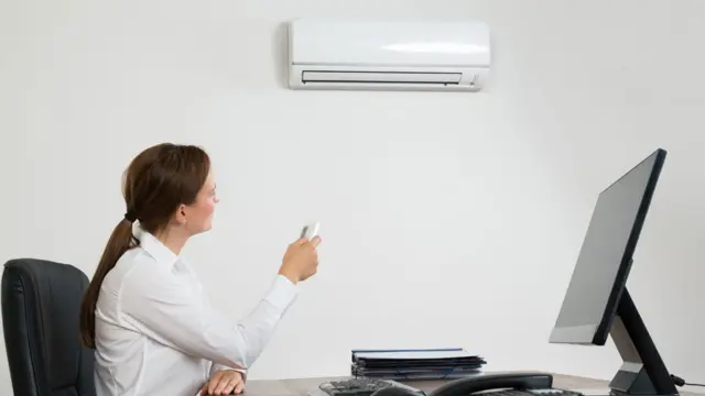 Mujer en una oficina ajustando el equipo de aire acondicionado con un control remoto