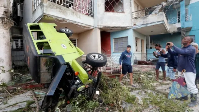 Personas fotografían un auto volcado afectado por el tornado.