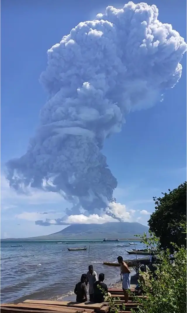 People watch a volcano spewing a huge column of ash