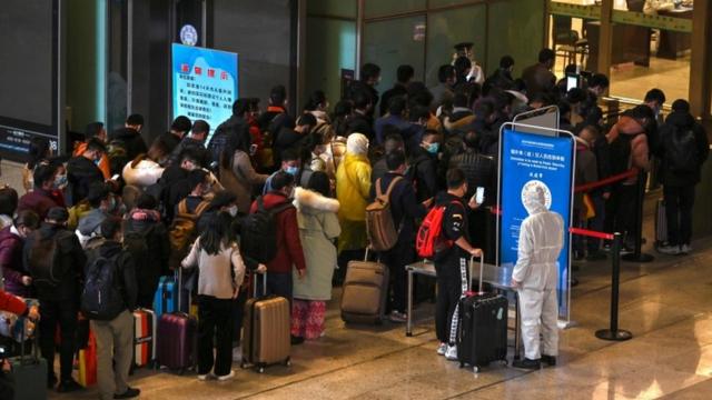 Mask-clad passengers wait in a line after arriving at the railway station in Wuhan, China's central Hubei province on 28 March 2020