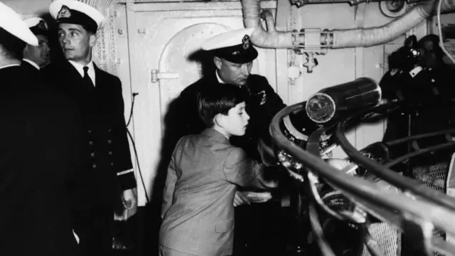 The young Prince Charles inspecting dummy shells pass by as Gunnery Instructor E H Bradley explains the working of a gun turret, aboard the HMS Eagle in Weymouth, April 29th 1959