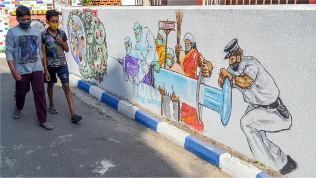Dos niños caminan junto a un mural de vacunación