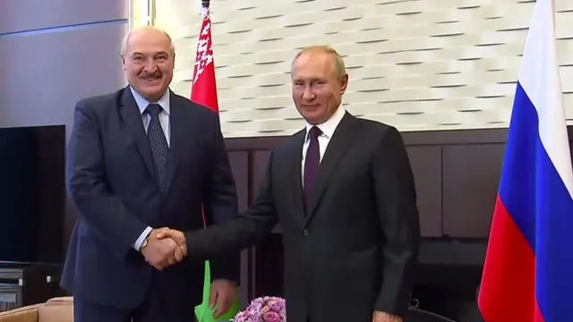 Lado a lado, Lukashenko e Vladimir Putin dão as mãos e sorriem para a câmera