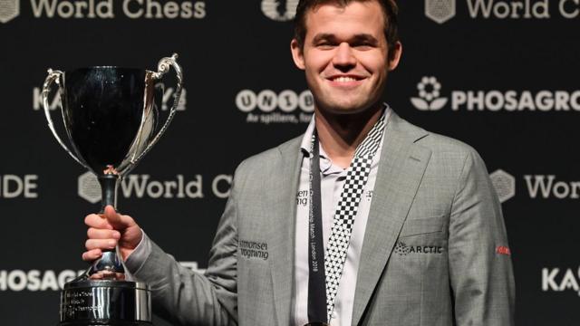 Magnus Carlsen sorri ao posar para foto e segurar troféu