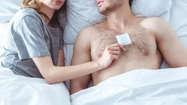 Pareja semidesnuda en la cama con un preservativo.