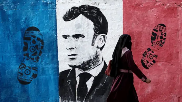 One Palestinian woman waka past one anti-French mural for Gaza City