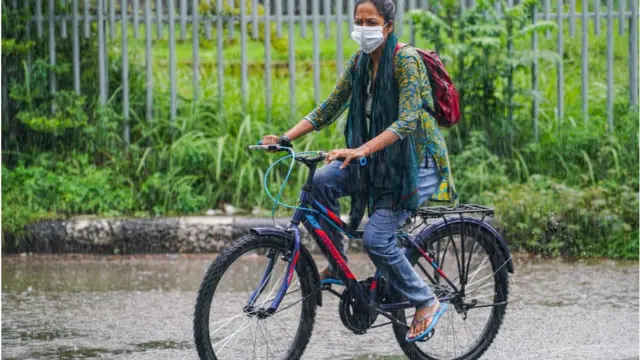 বৃষ্টিতে সাইকেল চালাচ্ছেন এক নারী।