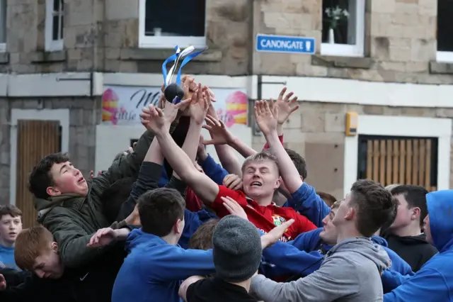 A crowd of people scramble to grab a leather ball in the street
