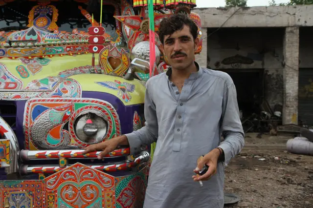 Vozač pozira ispred bogato ornamentisanog autobusa marke Bedford u Pešavaru, Pakistan. Ovakvi oslikani autobusi se širom Pakistana koriste kako za gradski, tako i na lokalnim međugradskim linijama.
