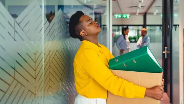 Mujer sostiene una caja llena de material de oficina.