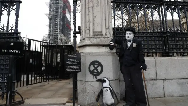 Westminister Sarayı'nın önünde Charlie Chaplin kostümü içindeki bir protestocu yanındaki penguen figürü ile birlikte.