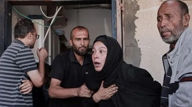 ग़ज़ा में हुए एक इसराइली हमले में अपने परिजनों को खोने वाली एक महिला के चेहरे पर दुख और हैरानी के भाव, उसे कुछ लोग सांत्वना देते हुए