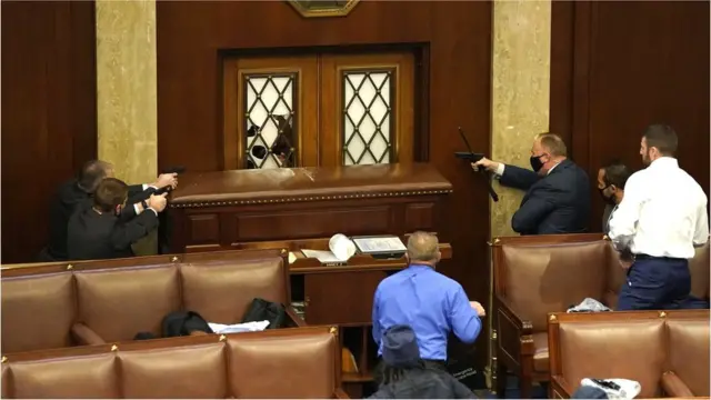 Law enforcement officers point their guns at a door that was vandalised in the House Chamber during a joint session of Congress in Washington DC, 6 January 2021