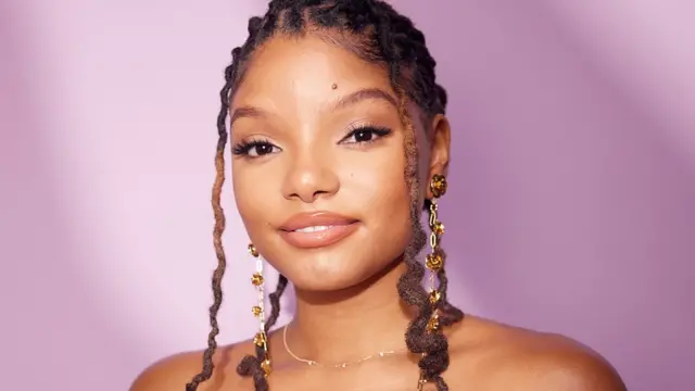 Halle Bailey, uma jovem negra com cabelo trançado e olhos castanhos amendoados, sorri para a câmera