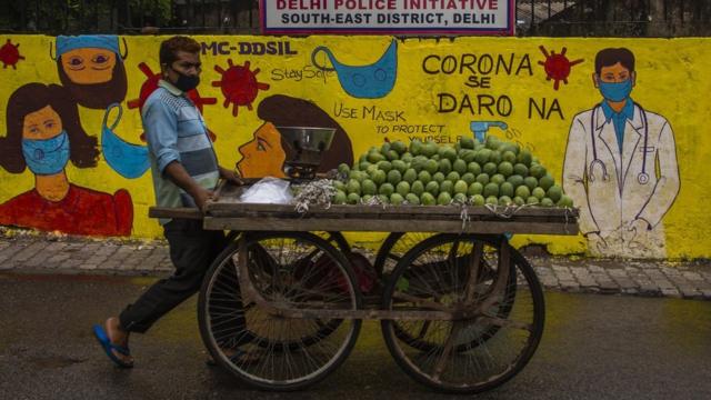 印度新德里街头一位小贩走过宣传防治COVID-19之壁画（17/7/2020）