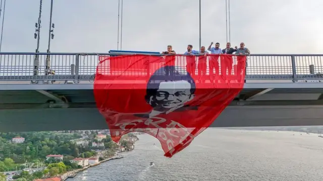 Altı kişi bir köprüde İmamoğlu'nun görselinin olduğu bir pankartı sallandırıyor.
