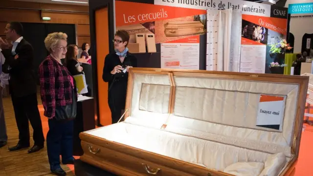 Em feira de convenções, mulher olha para caixão com frase "Me experimente"