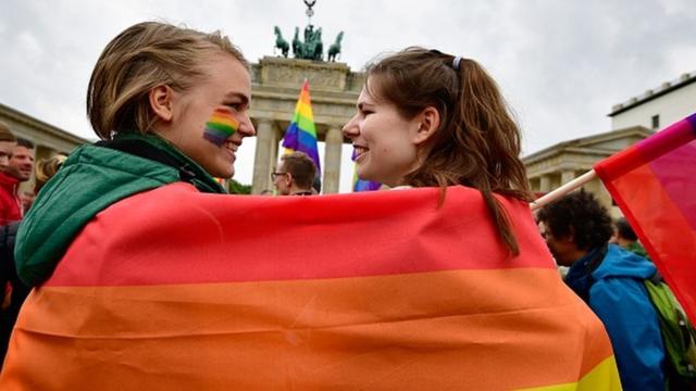 Two women are wrapped into a rainbow flag as they attend an LGBT rally in Berlin