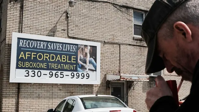 Un hombre enciende un cigarro frente a un anuncio de tratamiento médico