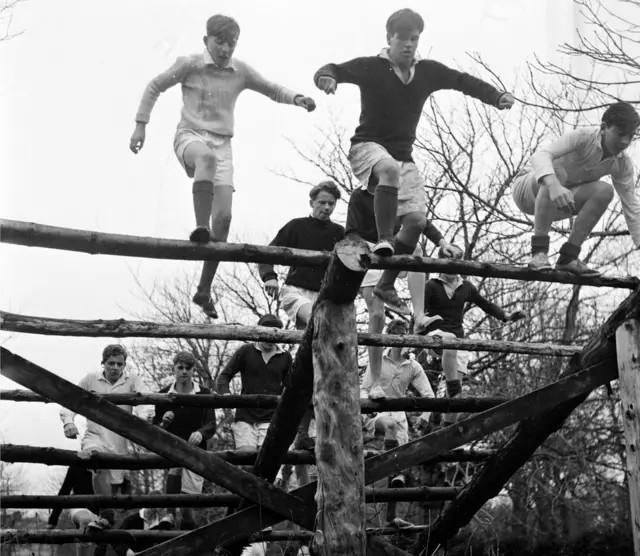 Photo en noir et blanc d'élèves de l'école Gordonstoun faisant de l'exercice physique sur un parcours d'obstacles en 1956.