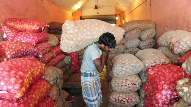 An Indian labourer carries bags of onions into a godown or warehouse at a wholesale market in Chennai on June 1, 2016.