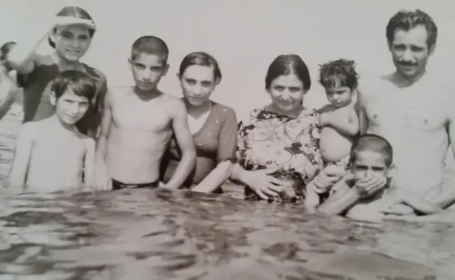Foto em preto e branco da família Kharaghani dentro do mar, na praia de Rasht, no Irã. Na imagem, aparecem Paknoosh, que fugiu para o Brasil em meio à guerra Irã-Iraque e à perseguição religiosa no Irã, com os irmãos e os pais
