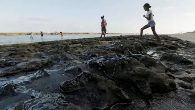 Focono funciona bwinóleo vazado sobre areia, com banhistas no planono funciona bwinfundo