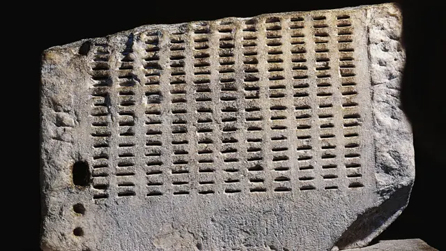 parte de uma kleroterion, uma pedra com diversos buracos no formato de linhas verticais