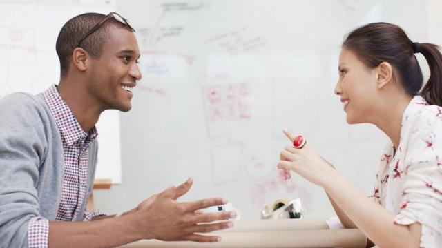 Um homem e uma mulher sorridentes conversando em um escritório