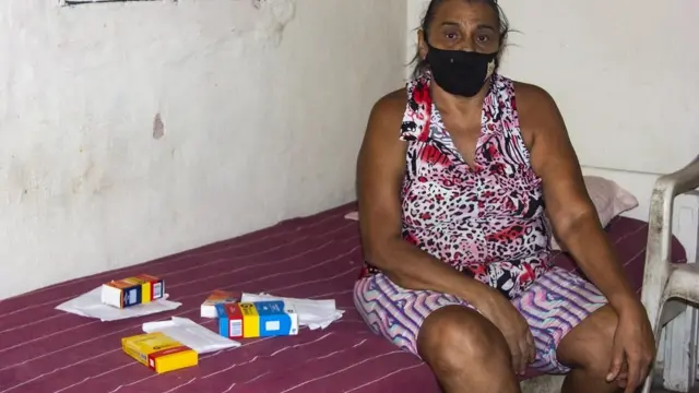 Senhora sentada na cama exibindo medicamentos