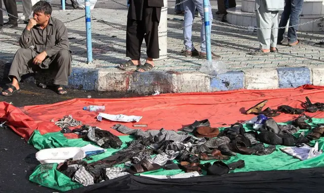 A man sits next to a blanket holding the possessions of people caught in a 2016 Kabul bombing