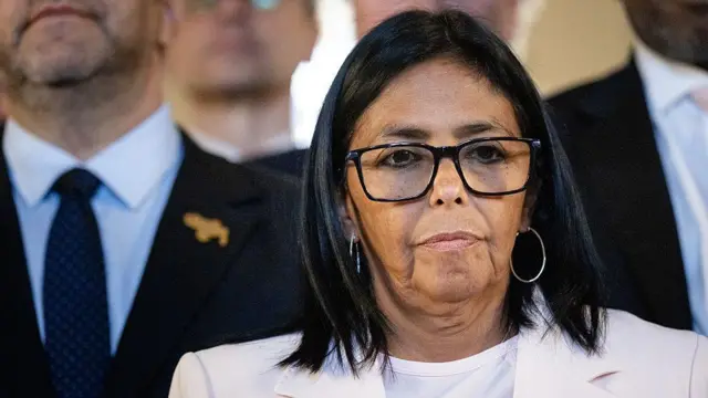 Delcy Rodríguez, vistiendo un traje blanco y gafas de montura negra.