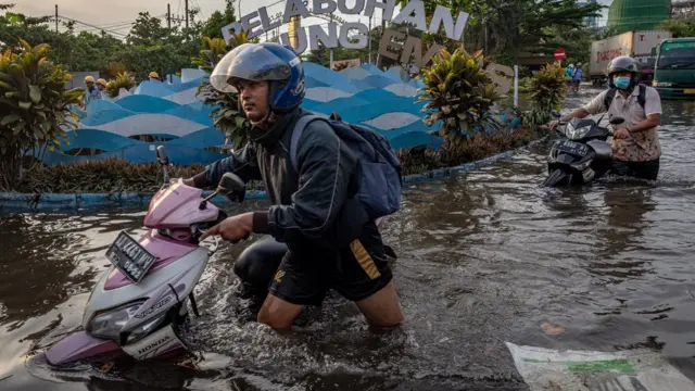 Sejumlah pekerja mendorong motornya yang mogok untuk menerobos banjir limpasan air laut ke daratan atau rob yang merendam kawasan Pelabuhan Tanjung Emas Semarang, Jawa Tengah, Senin (23/05)