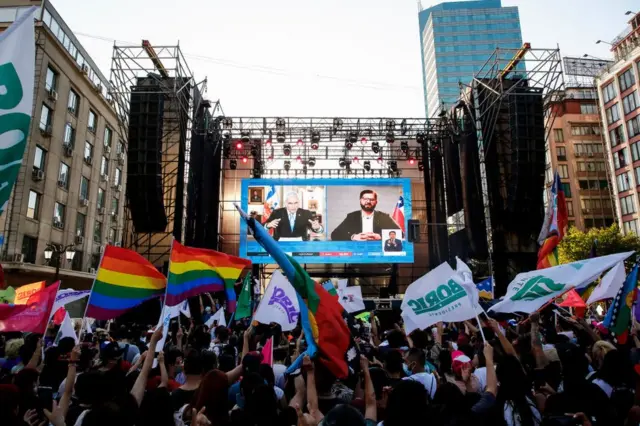 Partidarios de Gabriel Boric lo observan en videoconferencia junto al presidente saliente Sebastián Piñera.