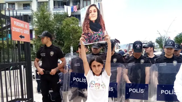Gülistan'ın ablası Aygül Doku, 2022 yılında bir eylem sırasında kardeşinin resmini taşıyor. Arkasında polisler var. 