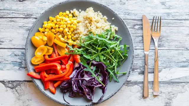 Plato de ensalada con arroz, maíz, lechuga, damascos y otros alimentos.