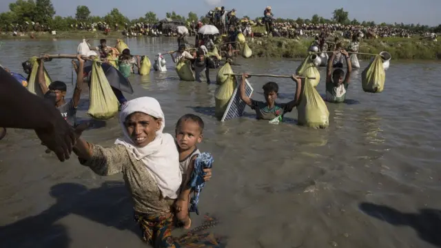 हाथ पकड़कर नदी से बाहर आती रोहिंग्या महिला