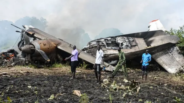 People stand near the cargo plane belonging to a local operator that crashed seven kilometres west of the Juba International airport shortly after takeoff on August 22, 2020, killing four passengers and three crew, with one survivor. - According to the Transport Minister Madut Biar Yol, the crew members were Russian while the passengers were all South Sudanese. The plane owned by local company South West Aviation had been carrying cash to the Wau region in the country's northwest for Juba-based Opportunity Bank.