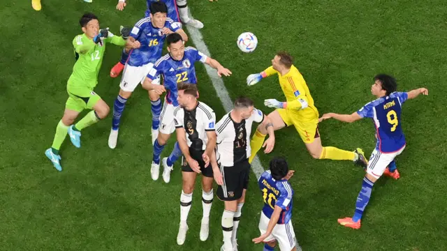 Uma foto aérea do goleiro da Alemanha pulando para cabecear contra o zagueiro do Japão Maya Yoshidabetsport comuma multidãobetsport comjogadoresbetsport comambas as equipes