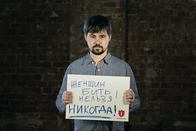 The musician Vasya Oblomov holds a card saying "You mustn't beat women! Ever!"
