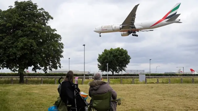 شخصان يشاهدان هبوط طائرة تابعة لشركة طيران الإمارات