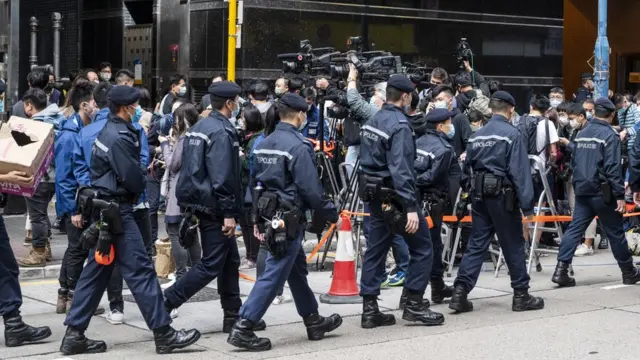 香港观塘《立场新闻》办公室所在大楼外一队警员列队走过媒体记者群（29/12/2021）