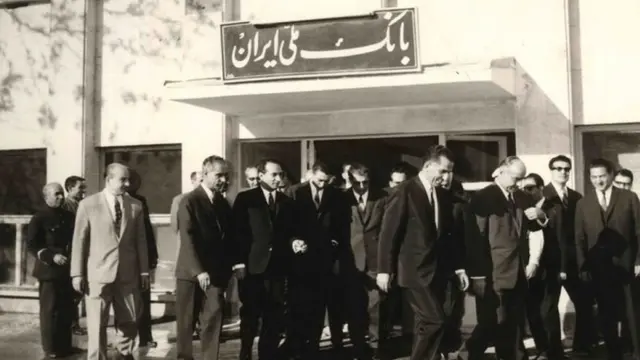 یوسف خوش کوش (نفر پنجم از راست که دستش را بالا گرفته) به همراه جمشید آموزگار در حال خروج از بانک ملی ایران. آقای خوش کوش در زمان نخست وزیر جمشید آموزگار به ریاست کل بانک مرکزی منصوب شد